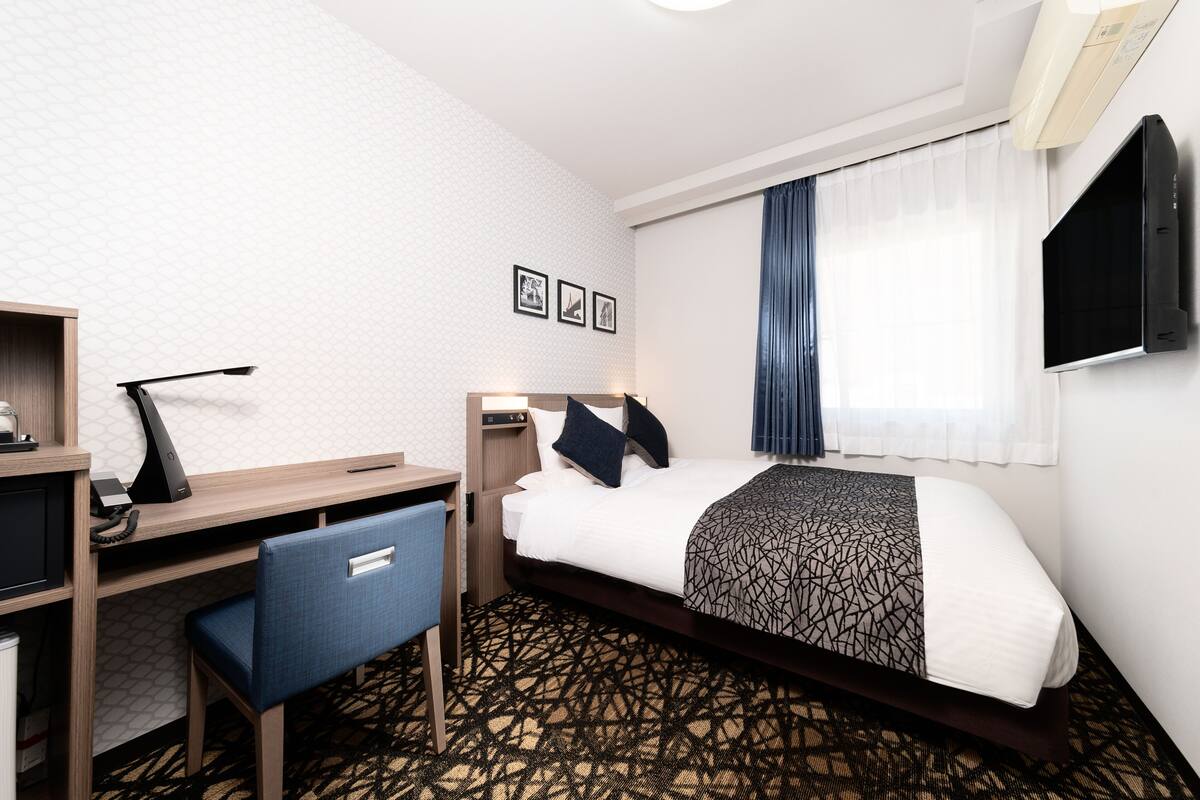 Ein Hotelzimmer mit Bett, Schreibtisch, Stuhl und einem kleinen Tisch mit Telefon.