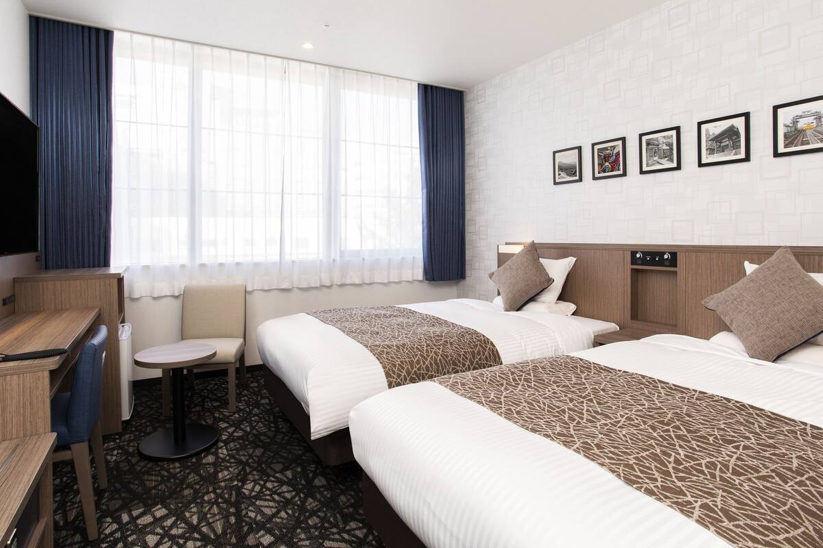 Ein Hotelzimmer mit zwei Betten, einem Schreibtisch, einem Stuhl und einem Fernseher.