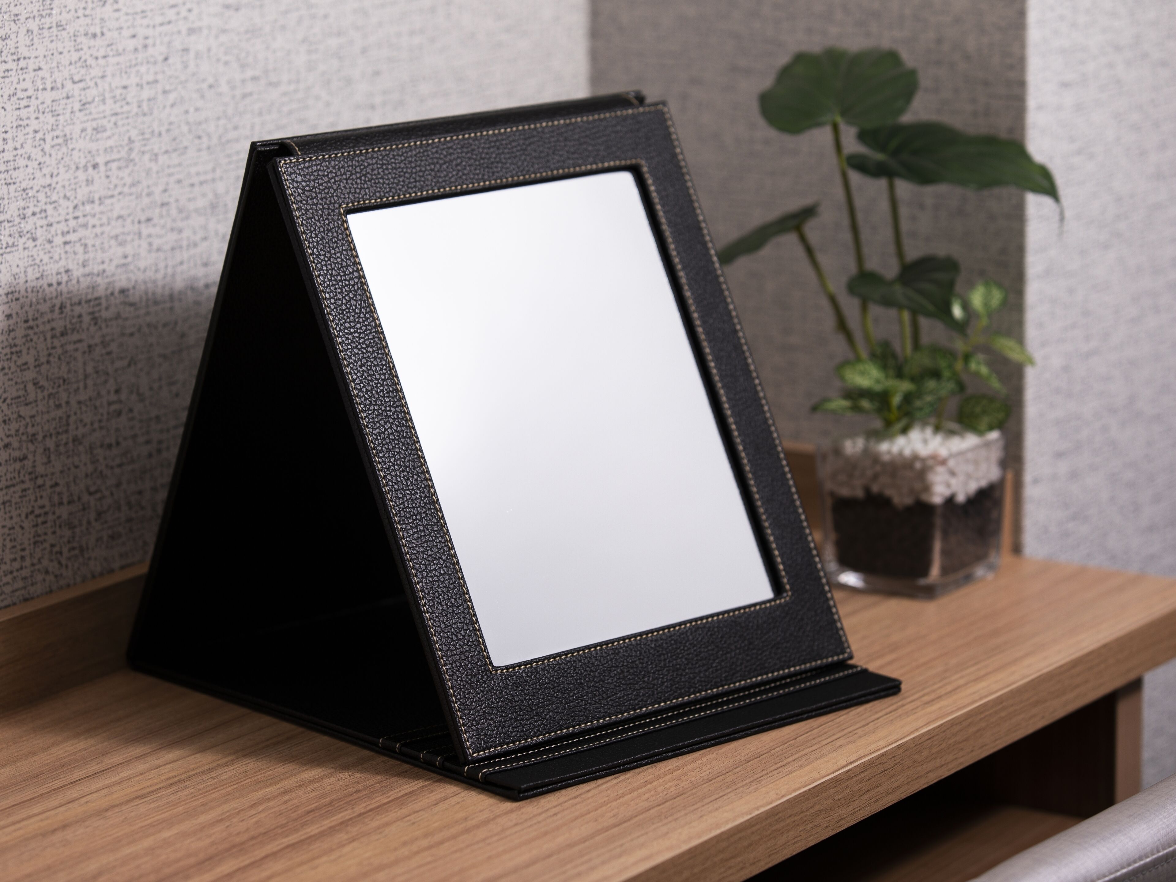 A black, textured, triangular stand holding a blank white sign, placed on a wooden surface with a potted plant in the background.