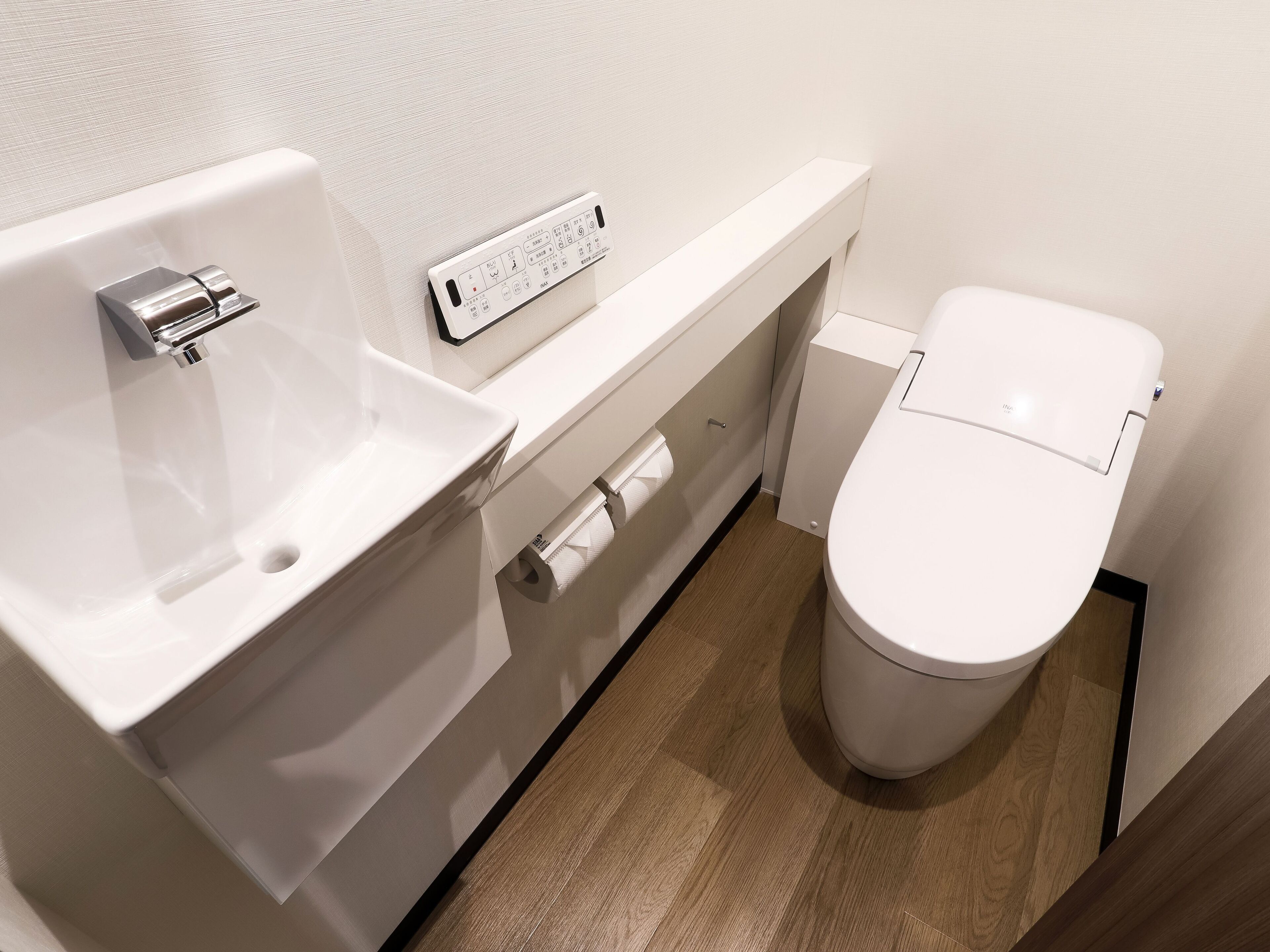 A modern bathroom with a white sink, toilet, and a control panel on the wall.