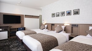 A hotel room with three beds, a flat-screen TV, a minibar, and a wall with framed pictures.