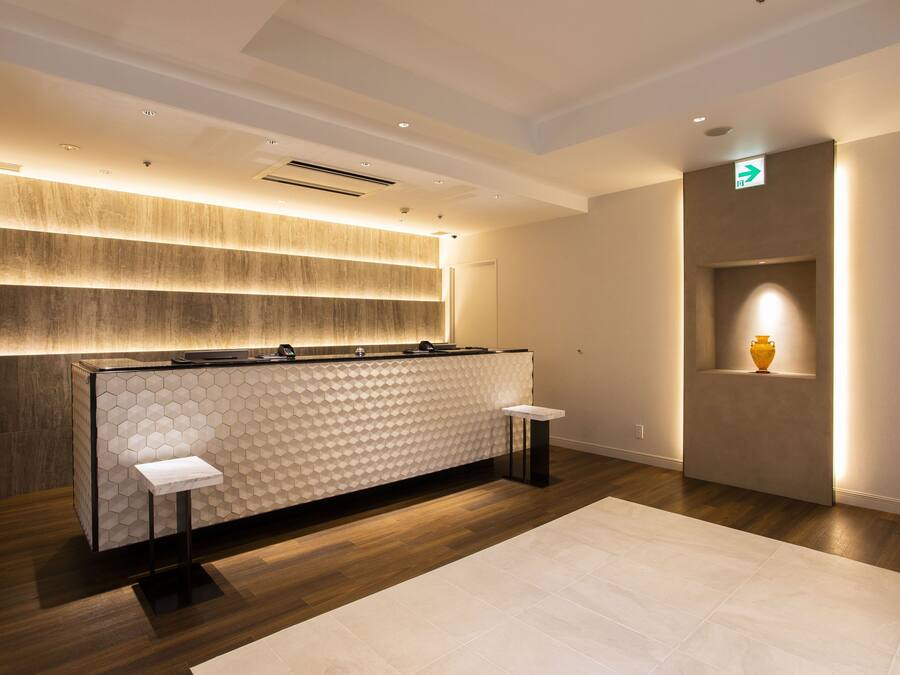 A reception area with a modern design, featuring a reception desk, a wall-mounted display, and a small shelf with a vase.