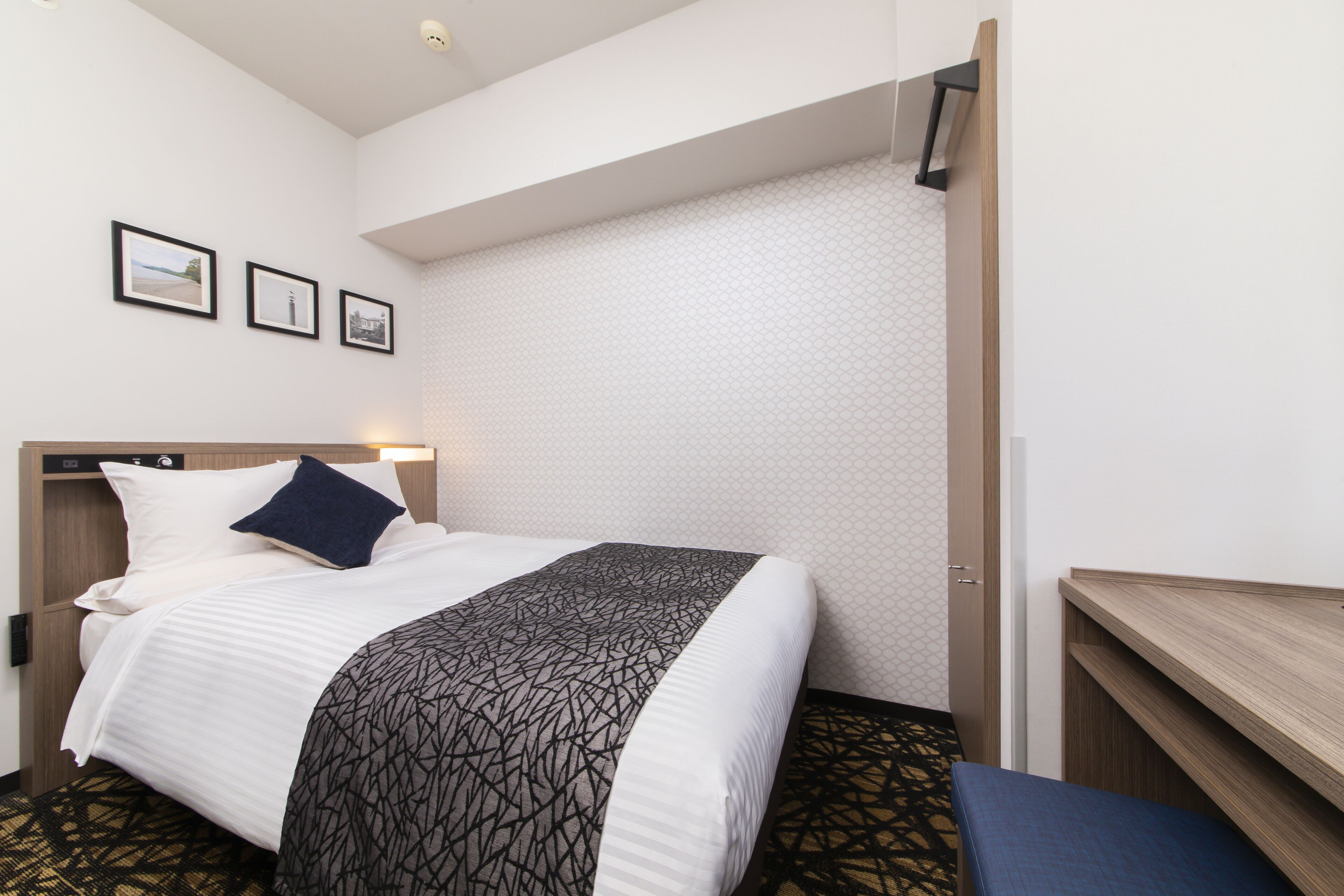 A hotel room with a bed, a desk, and a wall with three framed pictures.