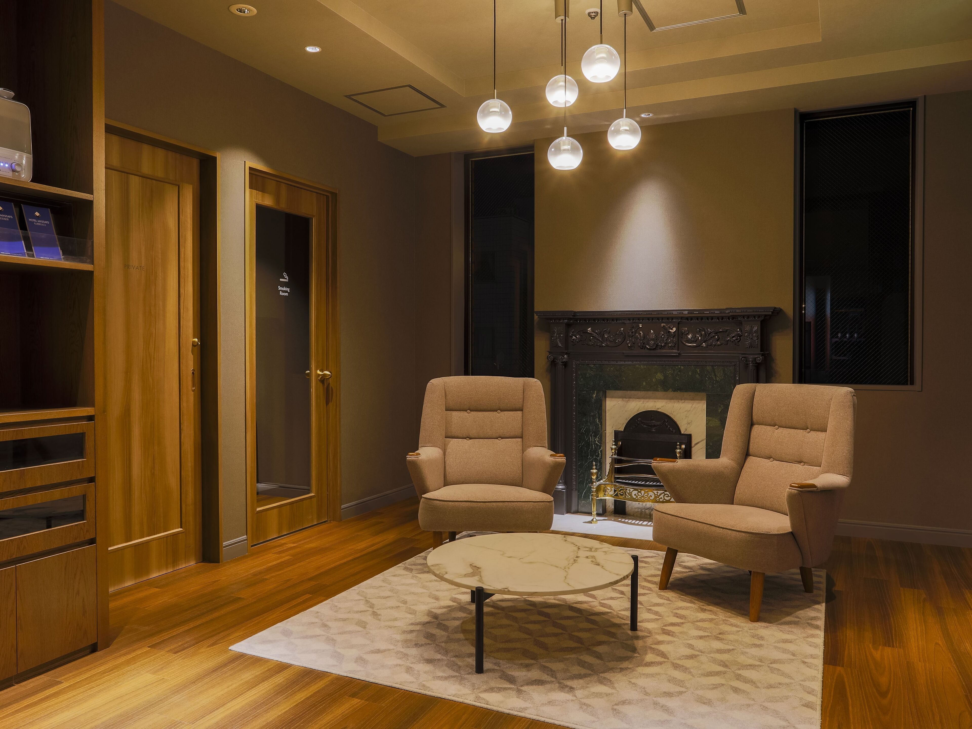 A modern living room with two armchairs, a round coffee table, a fireplace, and a bookshelf.