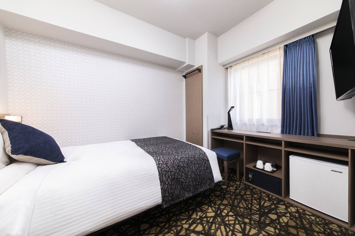 Ein Hotelzimmer mit einem Bett, einem Schreibtisch mit Stuhl, einem Fernseher und einem kleinen Kühlschrank.