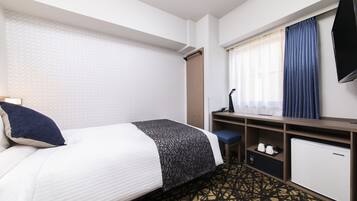 A hotel room with a bed, a desk with a chair, a television, and a small refrigerator.