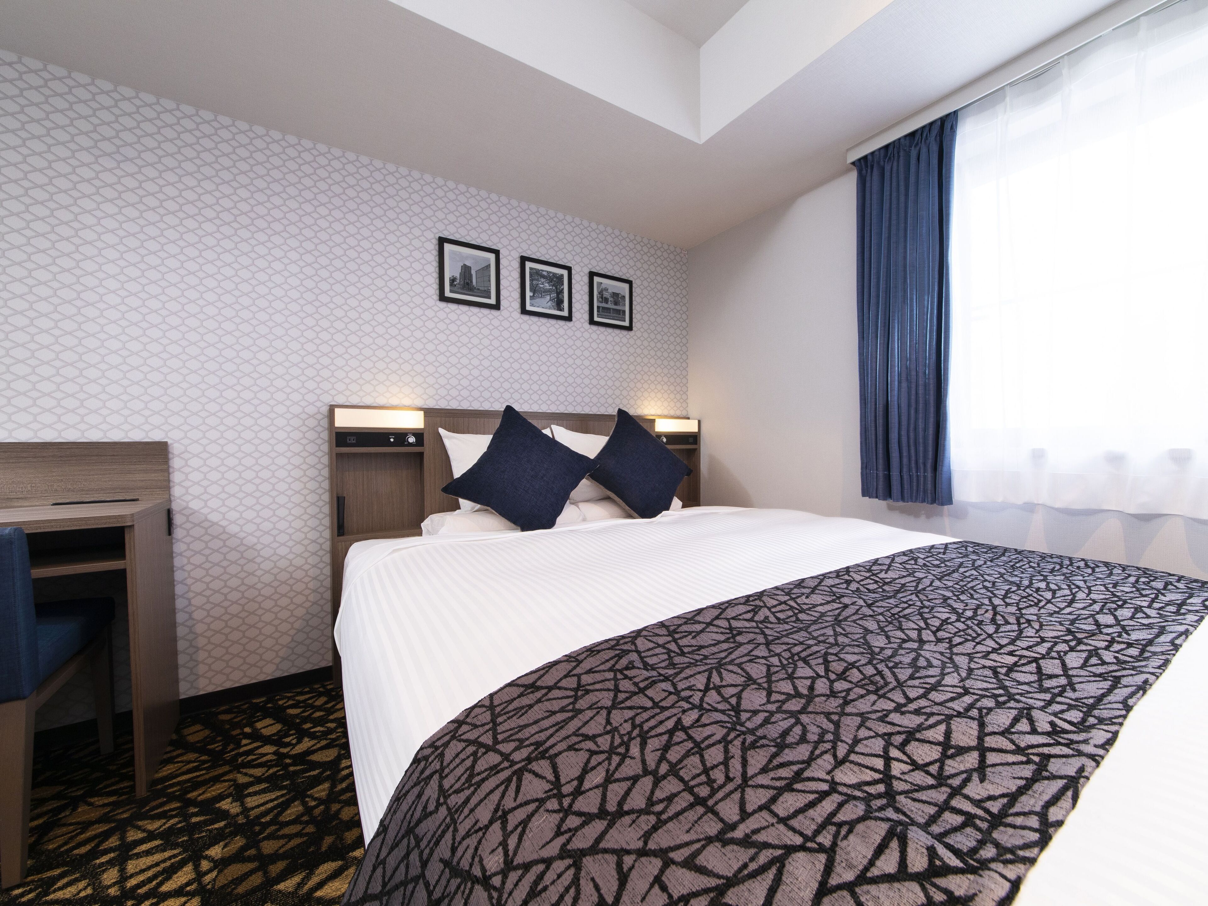 A hotel room with a bed, a desk, and a window with curtains.