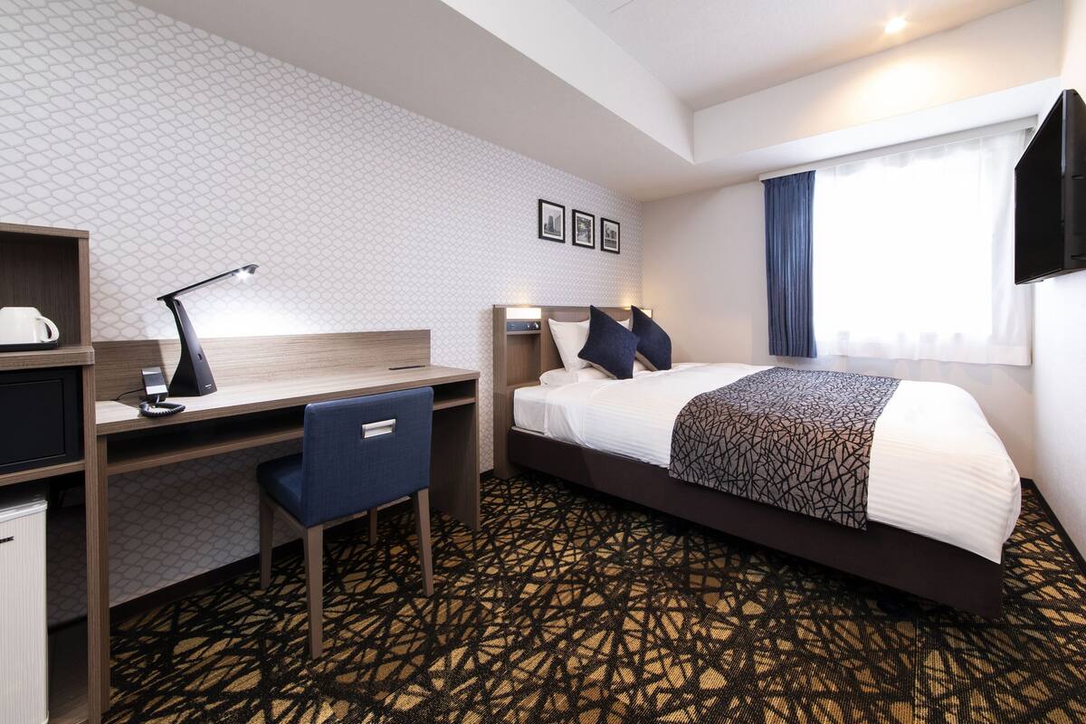 Ein Hotelzimmer mit Bett, Schreibtisch, Stuhl und einem gemusterten Teppich.
