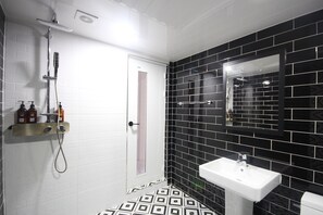 A bathroom with a white door, black tiled walls, a white sink, and a shower. - Gray Hotel (Busan)
