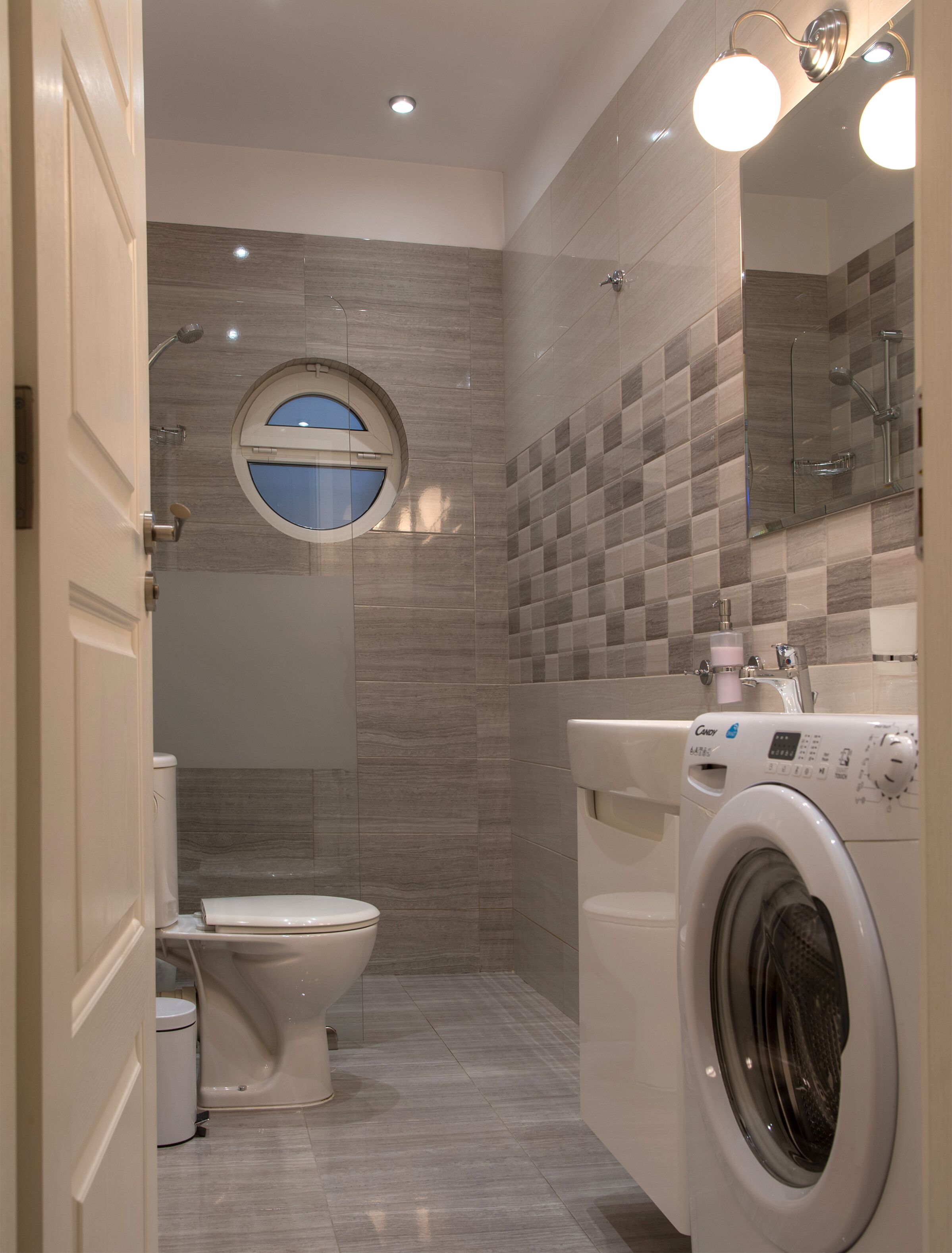 Un bagno compatto con il water, una lavatrice e uno specchio rotondo.