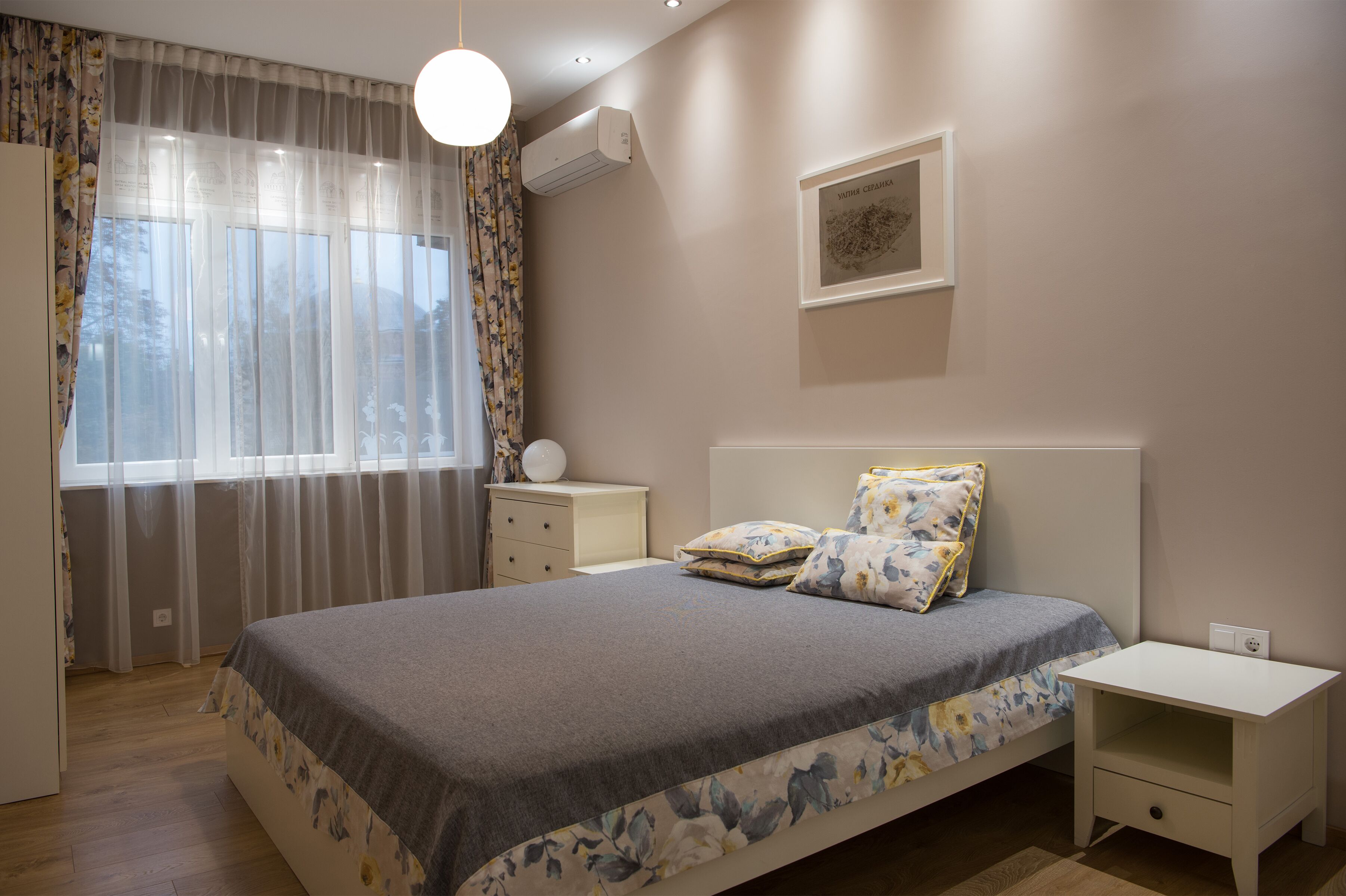 Un dormitorio con cama, mesita de noche, cortinas en la ventana y aire acondicionado instalado en la pared.