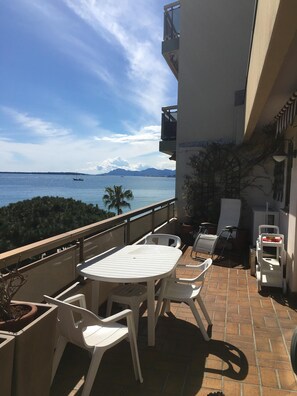 A balcony with a table and chairs, overlooking a body of water with a boat and mountains in the distance. - JUAN LES PINS STUDIO SEA VIEW (Juan Les Pins)