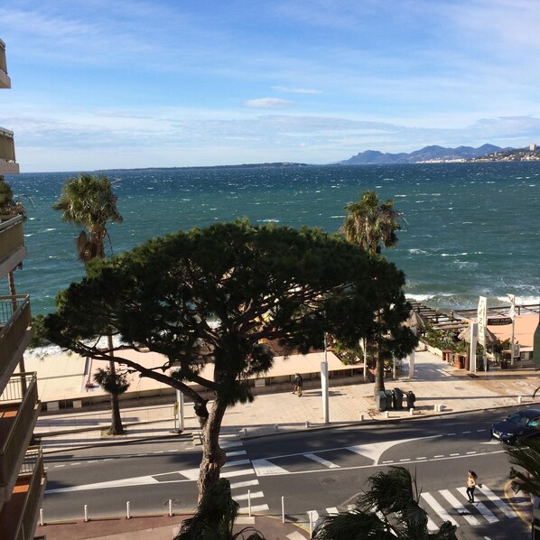 A coastal view with a tree-lined street and a building with a balcony overlooking the sea. - JUAN LES PINS STUDIO SEA VIEW (Juan Les Pins)