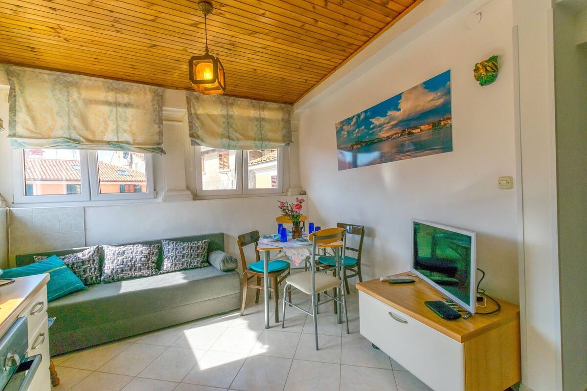 A cozy living area with a sofa, dining table, chairs, a TV, and a wooden ceiling.