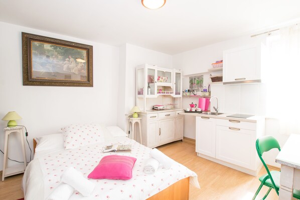 A compact hotel room with a bed, a small desk, a kitchenette, and a bathroom.