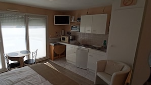 Une chambre d’hôtel de taille réduite, dotée d’une kitchenette, d’un petit coin repas et d’un lit.