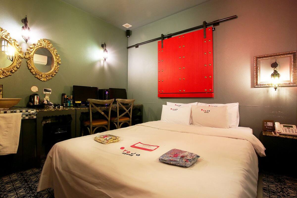 Een hotelkamer met een bed, een bureau, een stoel, een rode scheidingswand en een spiegel aan de muur.