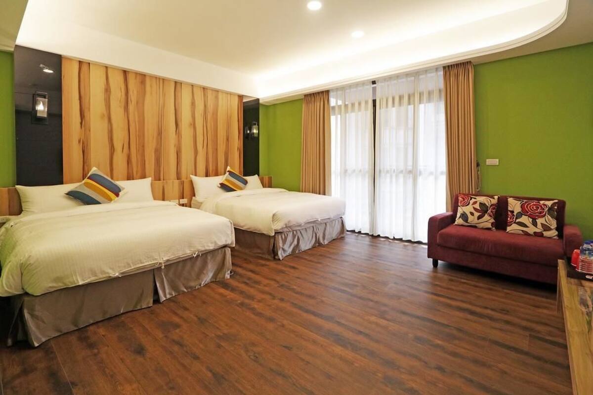 Ein Hotelzimmer mit zwei Betten, einem roten Sofa, Holzvertäfelung an der Wand und einem großen Fenster mit Vorhängen.