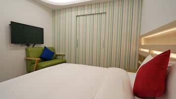 A modern hotel room with a large bed, a green armchair, a flat-screen TV mounted on the wall, and a striped wallpaper design.