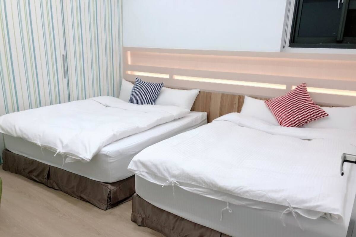 Zwei Einzelbetten mit weißer Bettwäsche, einem Streifenmuster-Vorhang und einem Holz-Kopfbrett.