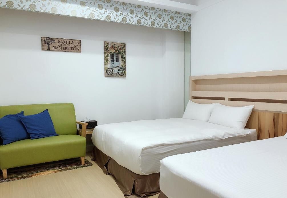 A hotel room with two beds, a green sofa, and decorative wall art.