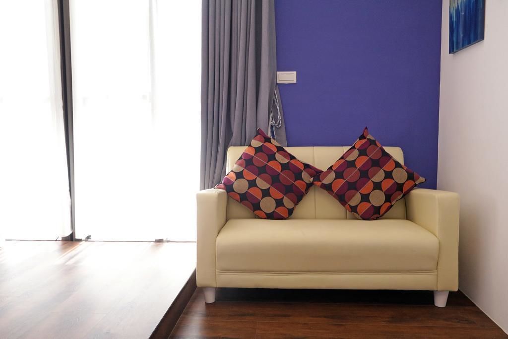 Ein cremefarbenes Sofa mit zwei gemusterten Kissen vor einer blauen Wand, einem grauen Vorhang und einem Holzboden.