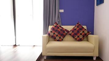 A cream-colored sofa with two patterned cushions against a blue wall, a grey curtain, and a wooden floor.