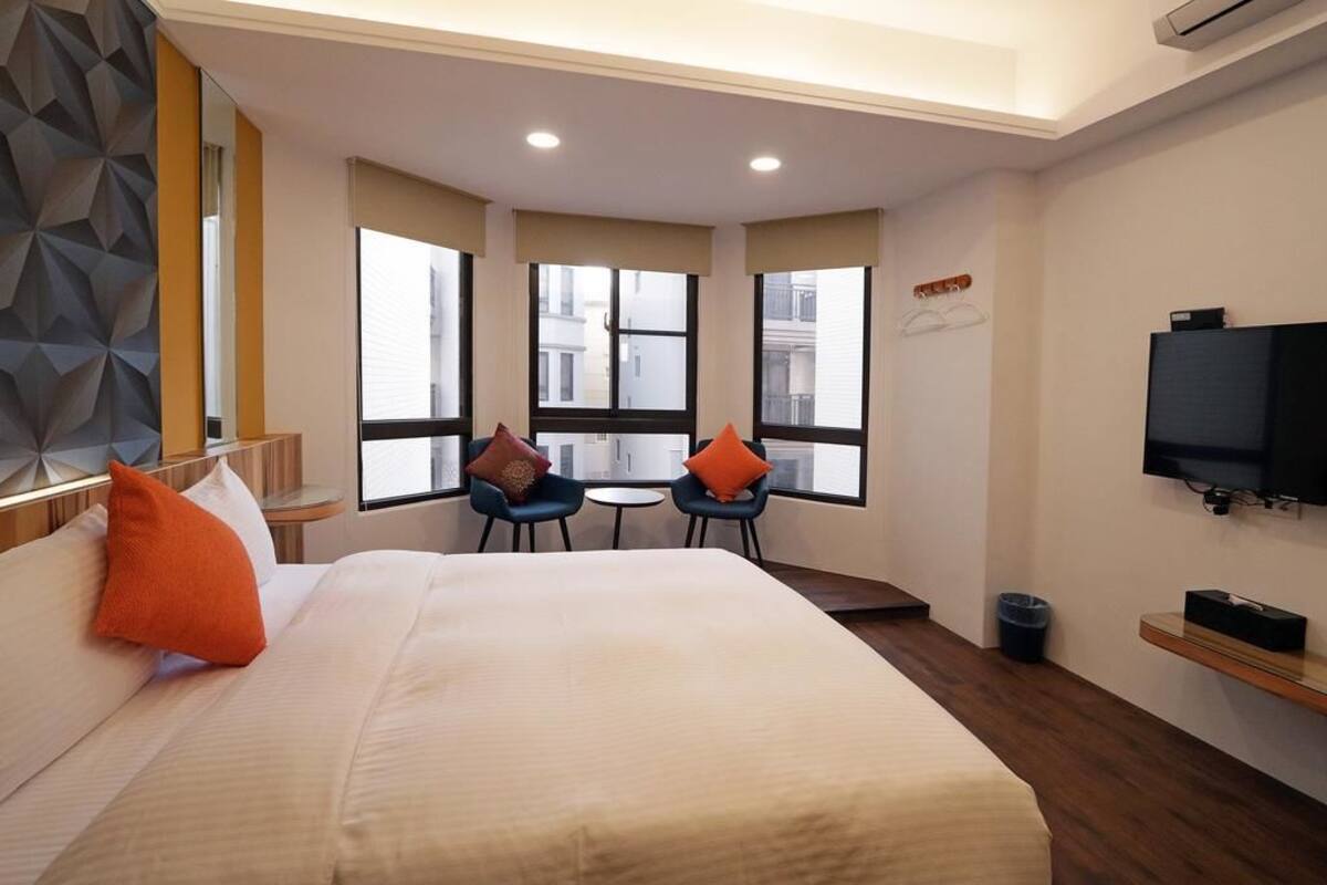 Ein Hotelzimmer mit einem großen Bett, zwei Sesseln, einem kleinen Tisch, einem Fernseher und großen Fenstern.