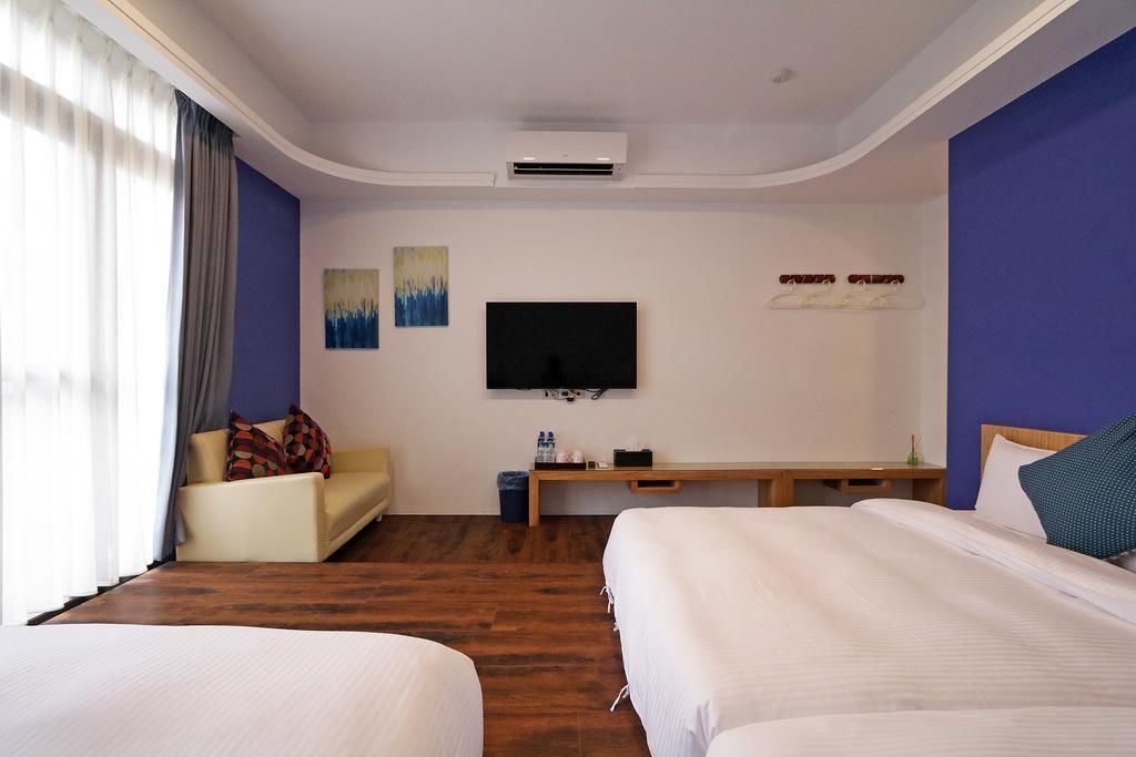 A hotel room with two beds, a sofa, a TV, and a desk.
