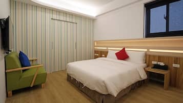 Une chambre d’hôtel avec un lit, un fauteuil vert, un téléviseur fixé au mur et une fenêtre avec des stores.