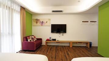 A room with a sofa, a TV mounted on the wall, a bench, and a bed.