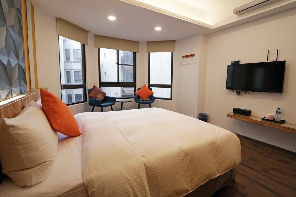 Una habitación de hotel con una cama, dos sillones, un televisor y un ventanal.