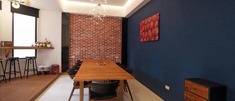 A modern dining area with a brick accent wall, a wooden table, and a dark blue wall with a red abstract painting.
