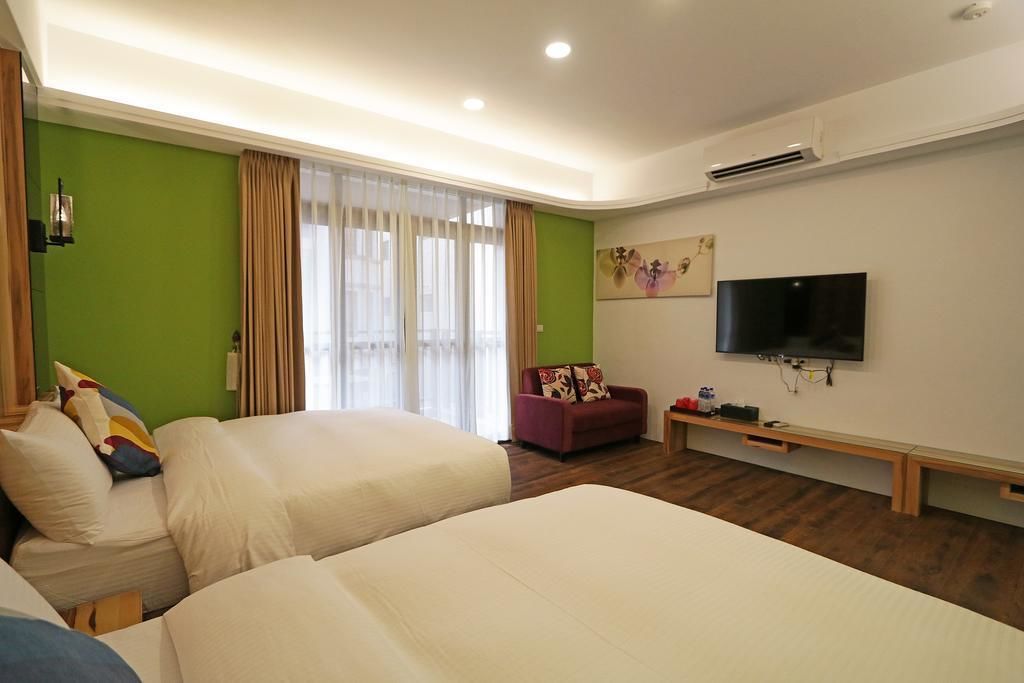 A hotel room with two beds, a TV, a sofa, and a window with curtains.