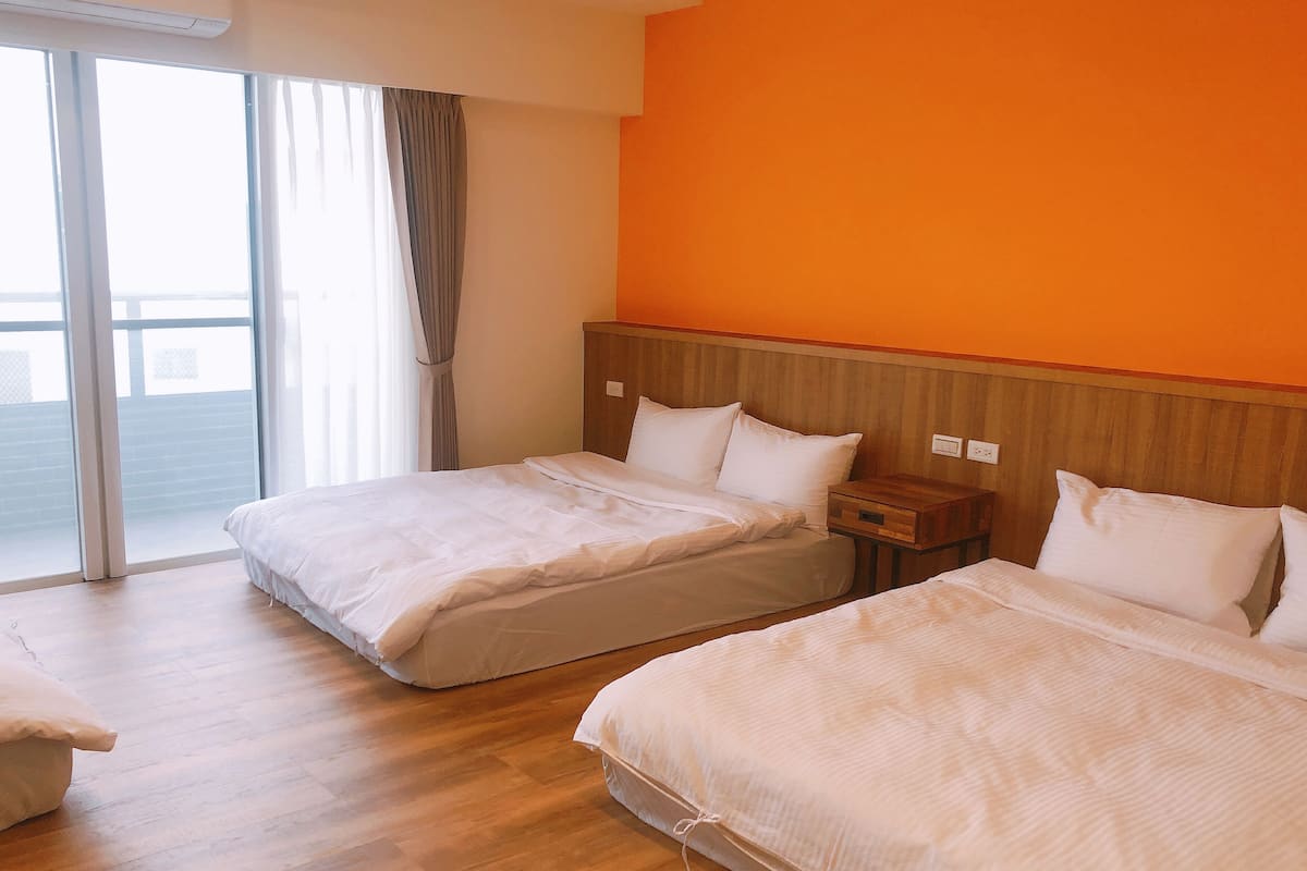 A hotel room with two beds, a wooden headboard, a nightstand, and a large window with curtains.