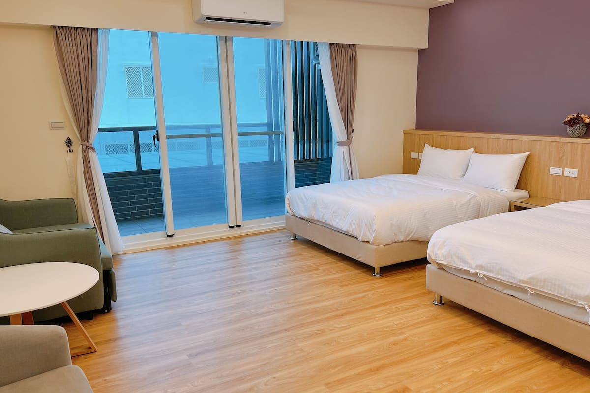 A hotel room with two beds, a small table, and a view of the sea through large glass doors.