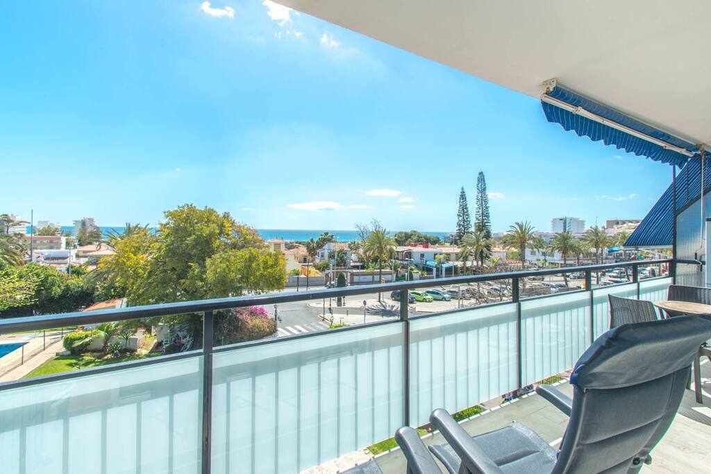 A balcony with a view of the sea, a pool, and surrounding buildings.