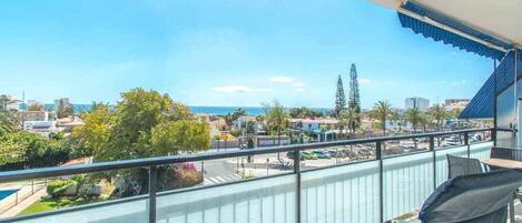 A balcony with a view of the sea, a pool, and surrounding buildings.