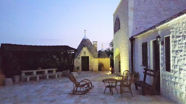 A courtyard with stone benches, a small building with a tiled roof, and a white wall with windows. - Dépendance in Villa Karmel (Cisternino)