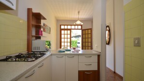 A compact kitchen with a gas stove, white cabinets, and a window with a view of greenery outside.