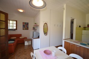 A compact living space with a sofa, a small table, a television, a mirror, and a kitchenette.