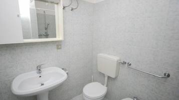 Un baño con lavamanos, inodoro y bidé blancos, paredes con azulejos y una ventana sobre el lavamanos.
