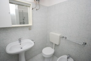 A bathroom with a white sink, toilet, and bidet, tiled walls, and a window above the sink.