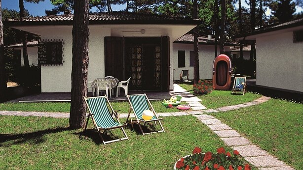 A house with a tiled roof, a front door, and a small porch with two green-striped lounge chairs and a table.