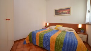 A bedroom with a bed, a nightstand, a wall-mounted painting, and a window with curtains.