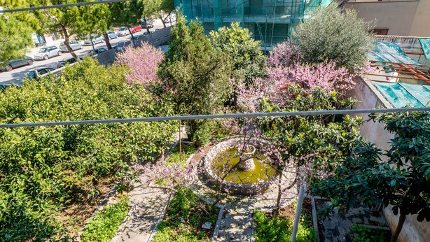 Une cour avec une fontaine, entourée d’arbres et d’arbustes, avec un bâtiment en arrière-plan.