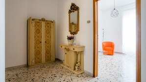 Une pièce comprenant une grande armoire, une coiffeuse avec un miroir, une petite table avec un vase et une chaise orange.