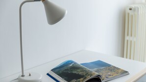 Un bureau avec une lampe blanche et un magazine ouvert posé dessus.