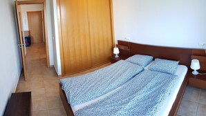 A bedroom with a large bed, a wooden wardrobe, a bedside table with a lamp, and a tiled floor. - La Tejita - with two terraces depending on the direction of wind and sun. (Los Abrigos)