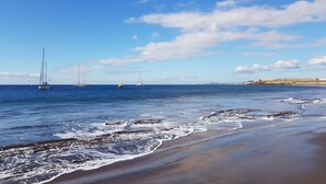 A beach with waves, a sandy shore, and sailboats in the distance. - La Tejita - with two terraces depending on the direction of wind and sun. (Los Abrigos)